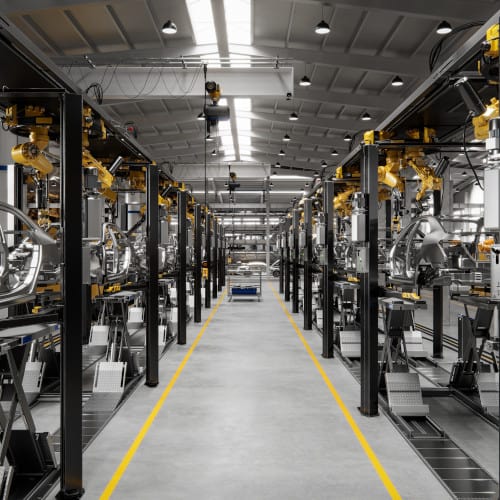 Industrial factory interior with automated machinery and equipment aligned along both sides of a central aisle marked by yellow lines.